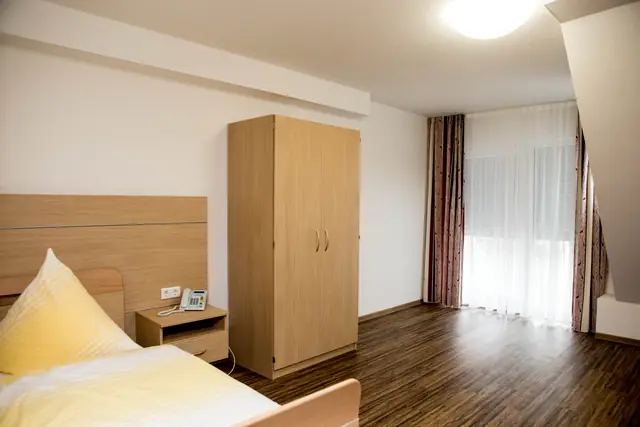 Einzelzimmer mit Bett, Kleiderschrank und Holzboden